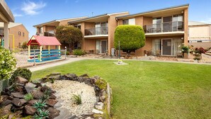 A multi-story residential building with a well-maintained lawn, a small play area, and a variety of plants and shrubs.