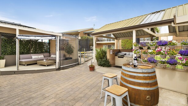 An outdoor patio area with a covered seating area, a bar with a wooden barrel, and potted plants. - Marine Cove Resort (Goolwa South)