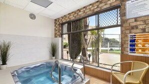 A spa pool area with a hot tub, a chair, and a window with a view of the outdoors. - Marine Cove Resort (Goolwa South)
