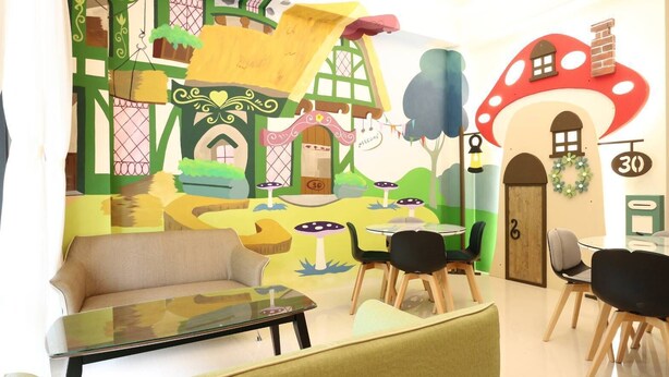Un salón infantil con un mural, un sofá, una mesa de centro y varias sillas.
