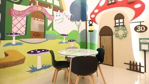 Una sala de juegos infantiles con un mural temático de setas, una mesa redonda con sillas y una puerta con el número 30.