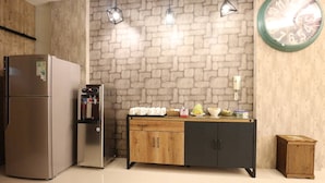 Una cocina con refrigerador, cafetera, armario de madera y un reloj en la pared.