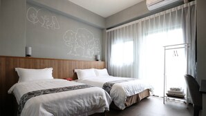 Habitación de hotel con dos camas, cabecero de madera, un ventanal grande con cortinas translúcidas y una pared con ilustraciones de árboles.