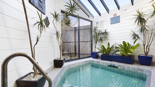 An indoor swimming pool with tiled walls, potted plants, and a clear glass door. - Whitecliffs Beach Resort (Rye)