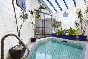 An indoor swimming pool with tiled walls, potted plants, and a clear glass door. - Whitecliffs Beach Resort (Rye)