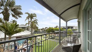 A balcony with a view of a swimming pool, palm trees, and a grassy yard. - Whitecliffs Beach Resort (Rye)