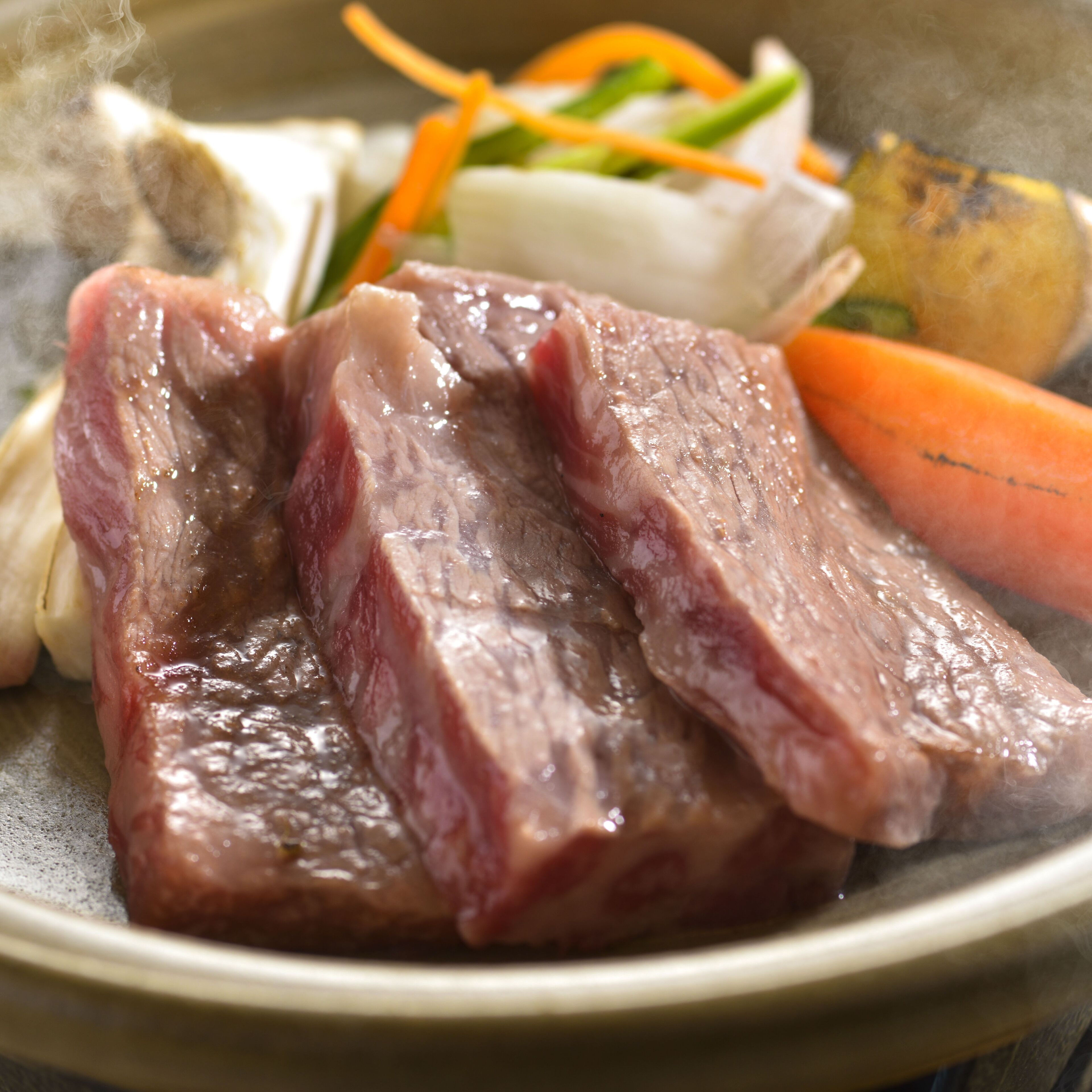 A plate with raw beef, vegetables, and a white item, possibly a dumpling or bread.