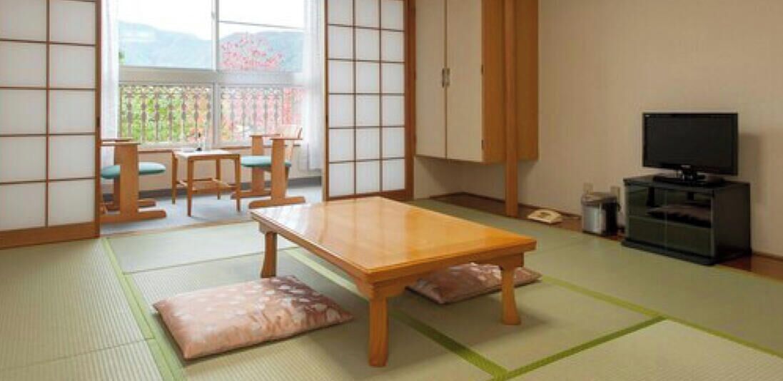 A traditional Japanese room with tatami flooring, a low table, a television, and sliding doors.