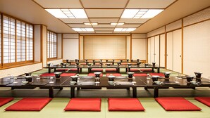 Perinteinen japanilaistyylinen kokoushuone, jossa on tatamimatot lattialla, matalat pöydät ja punaiset tyynyt.