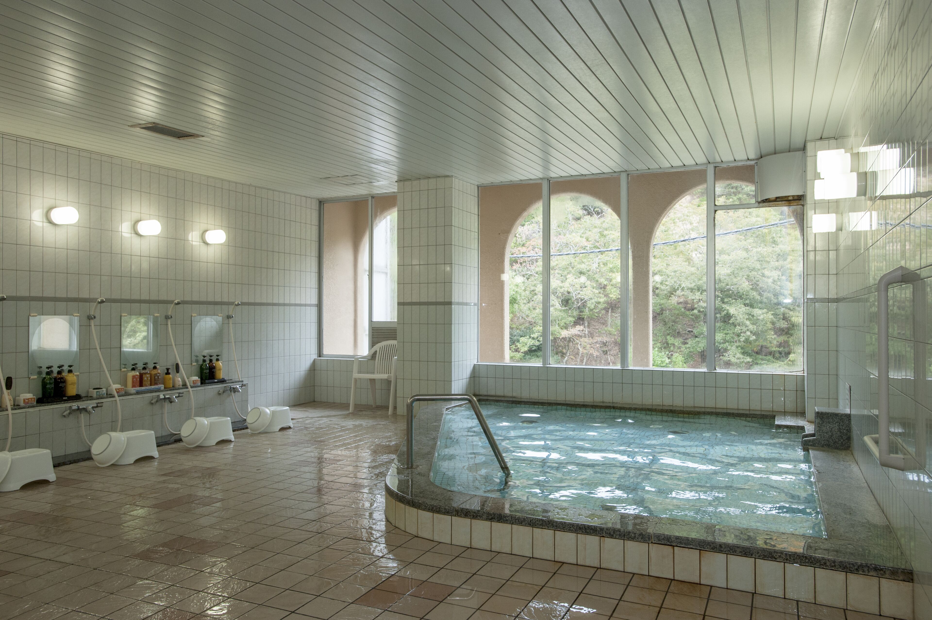 A large indoor swimming pool with a tiled floor, a jacuzzi, and a row of sinks and mirrors.