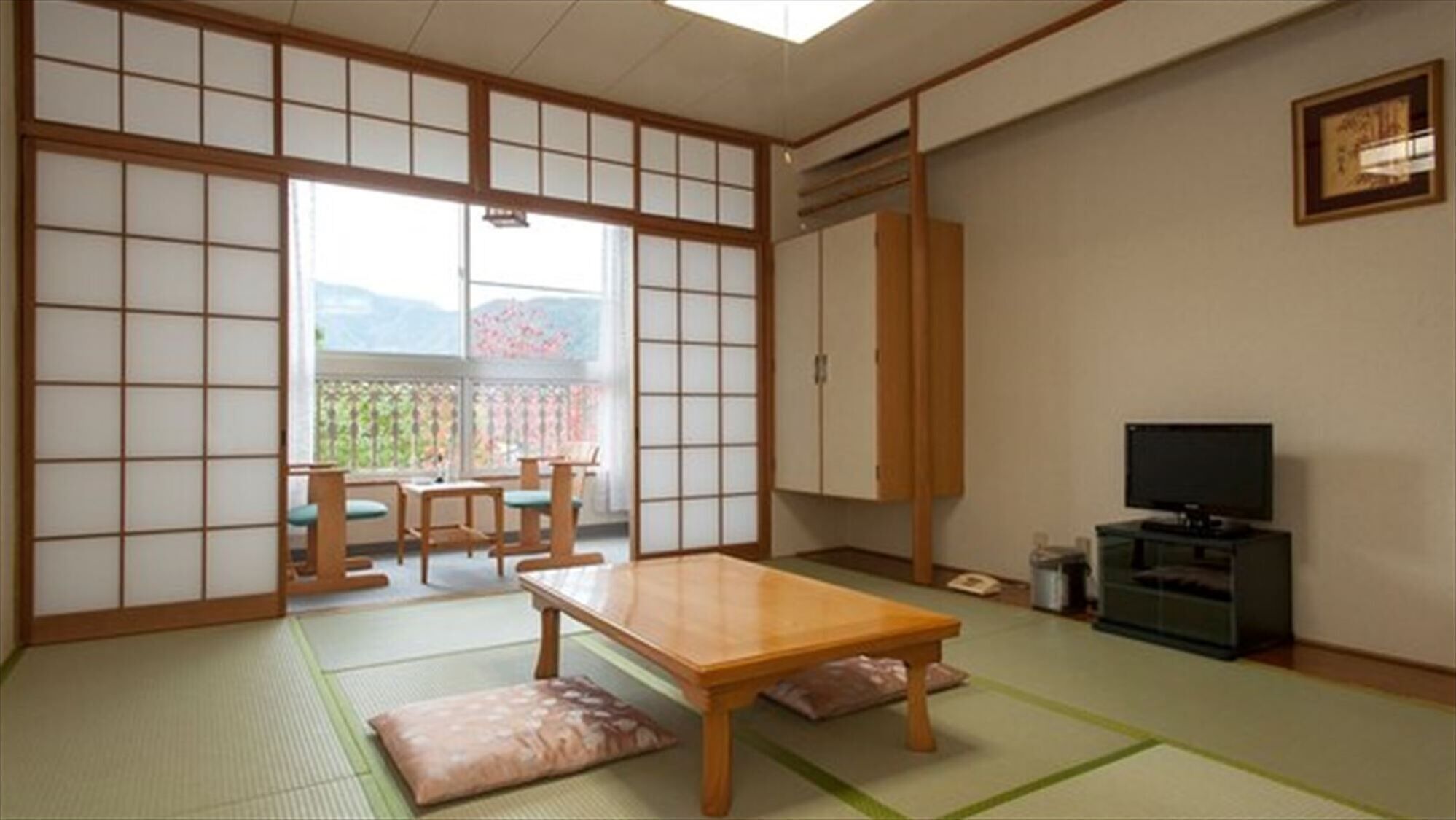 A traditional Japanese room with tatami flooring, a low table, a TV, and sliding doors.