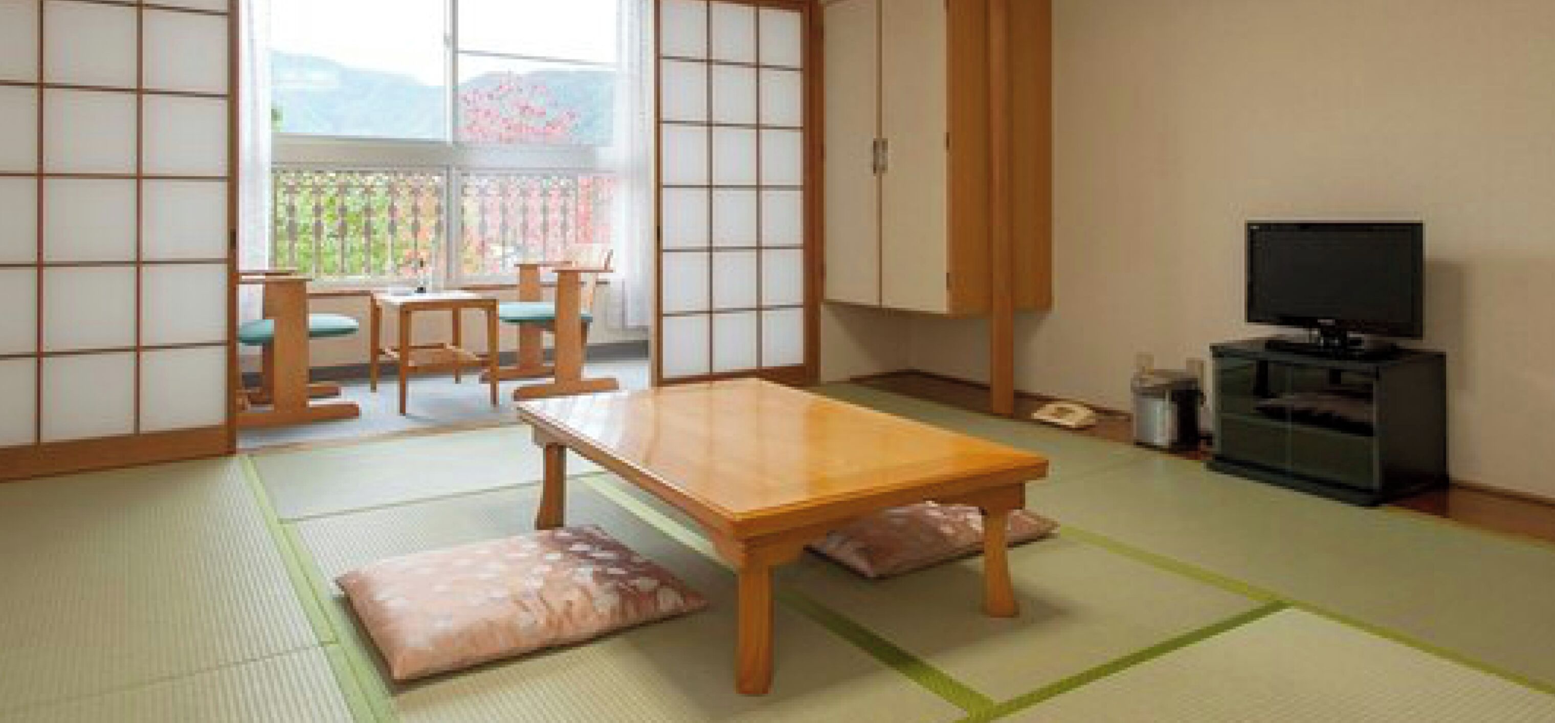 A traditional Japanese room with tatami flooring, a low wooden table, a television, and sliding doors.