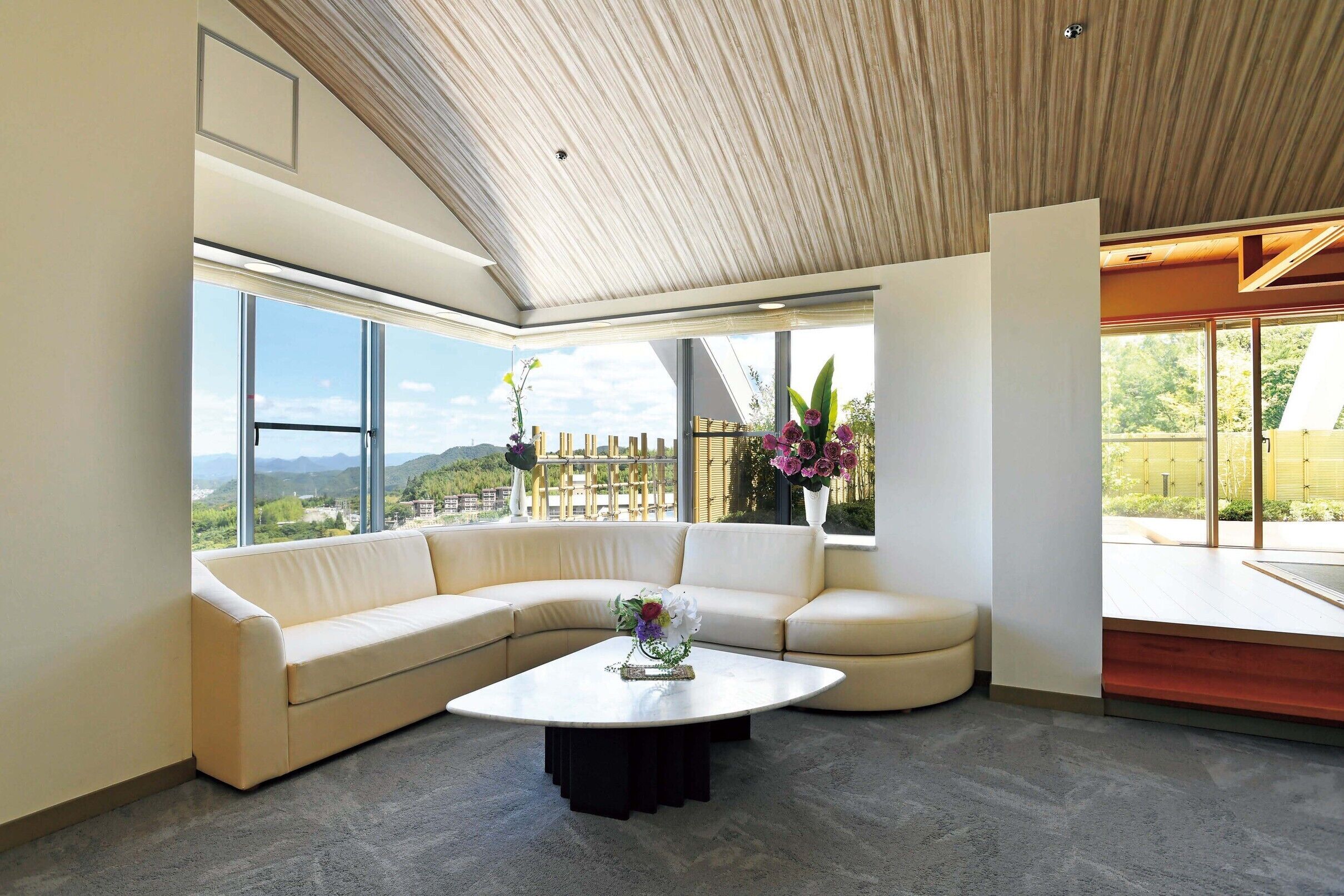 A modern living room with a curved sofa, a round coffee table, large windows, and a view of the outdoors.
