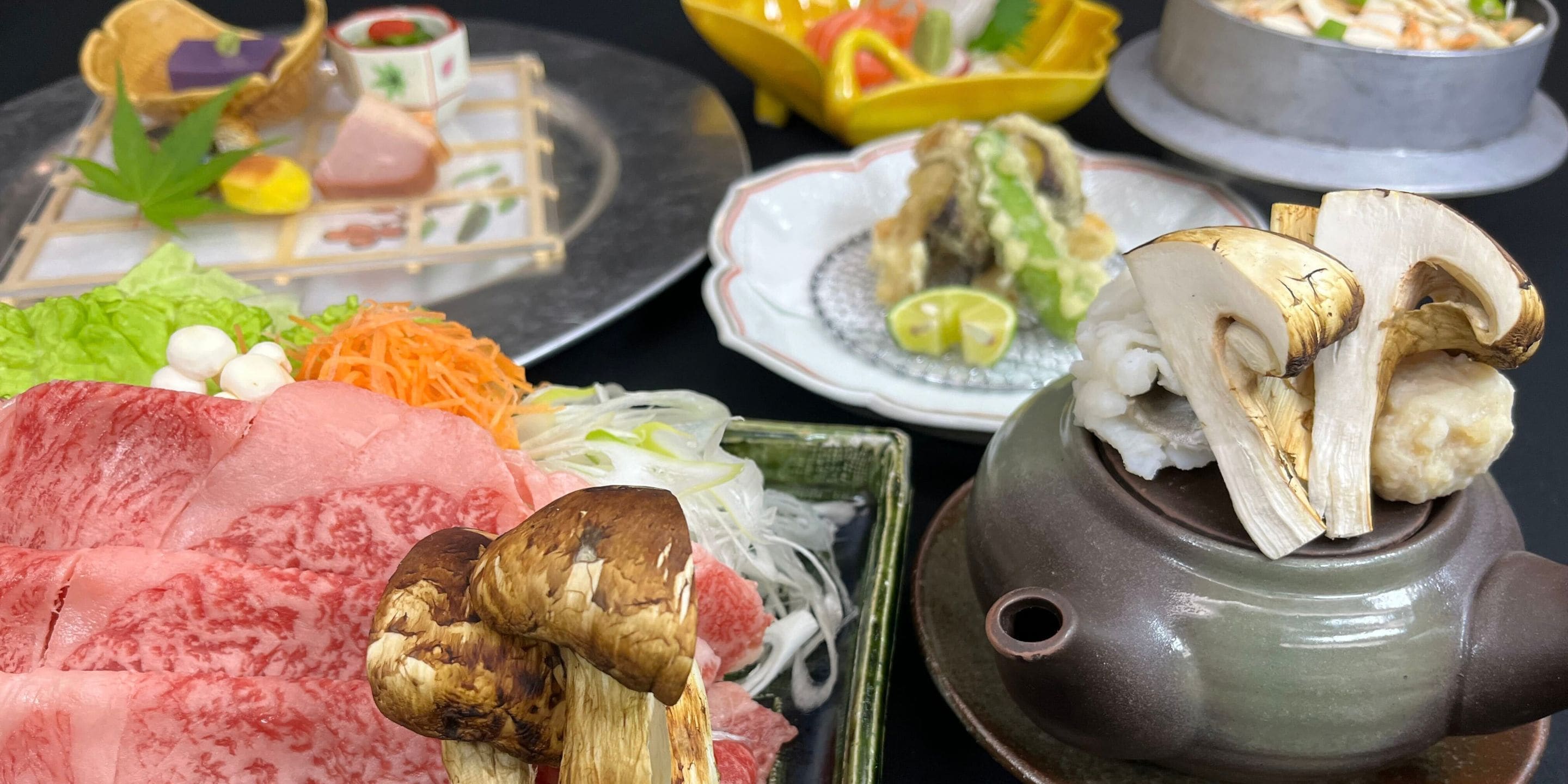 A variety of food items including sliced meat, vegetables, and mushrooms, arranged on a table with a teapot.