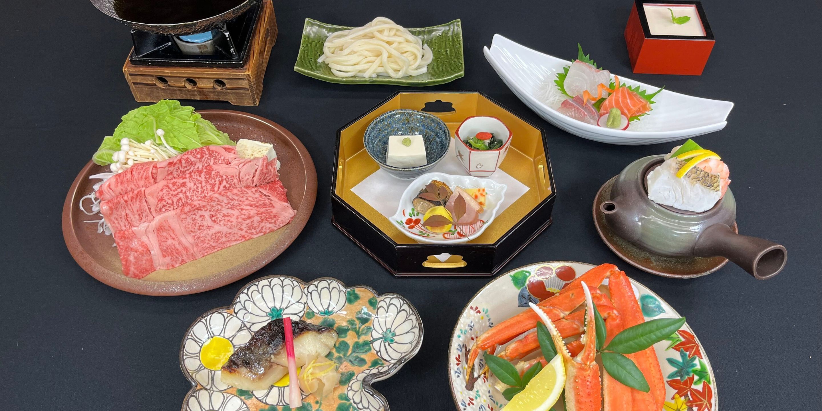 A variety of Japanese dishes including sashimi, seafood, and a hot pot setup.