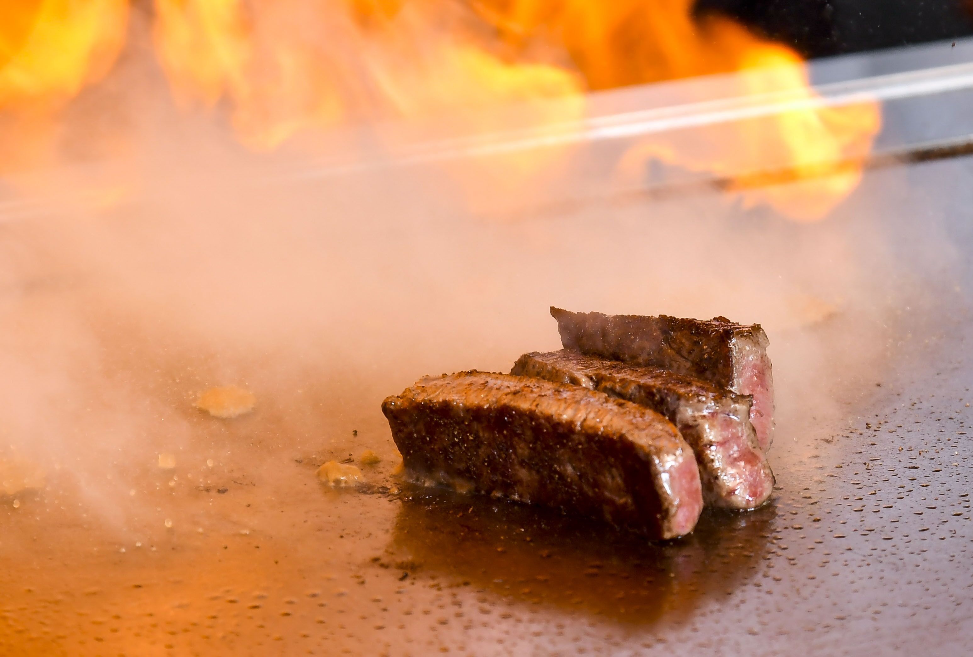 Un filete cocinándose en una parrilla, con llamas visibles al fondo.