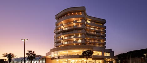 A multi-story hotel with a curved facade, balconies on each floor, and a glass entrance.