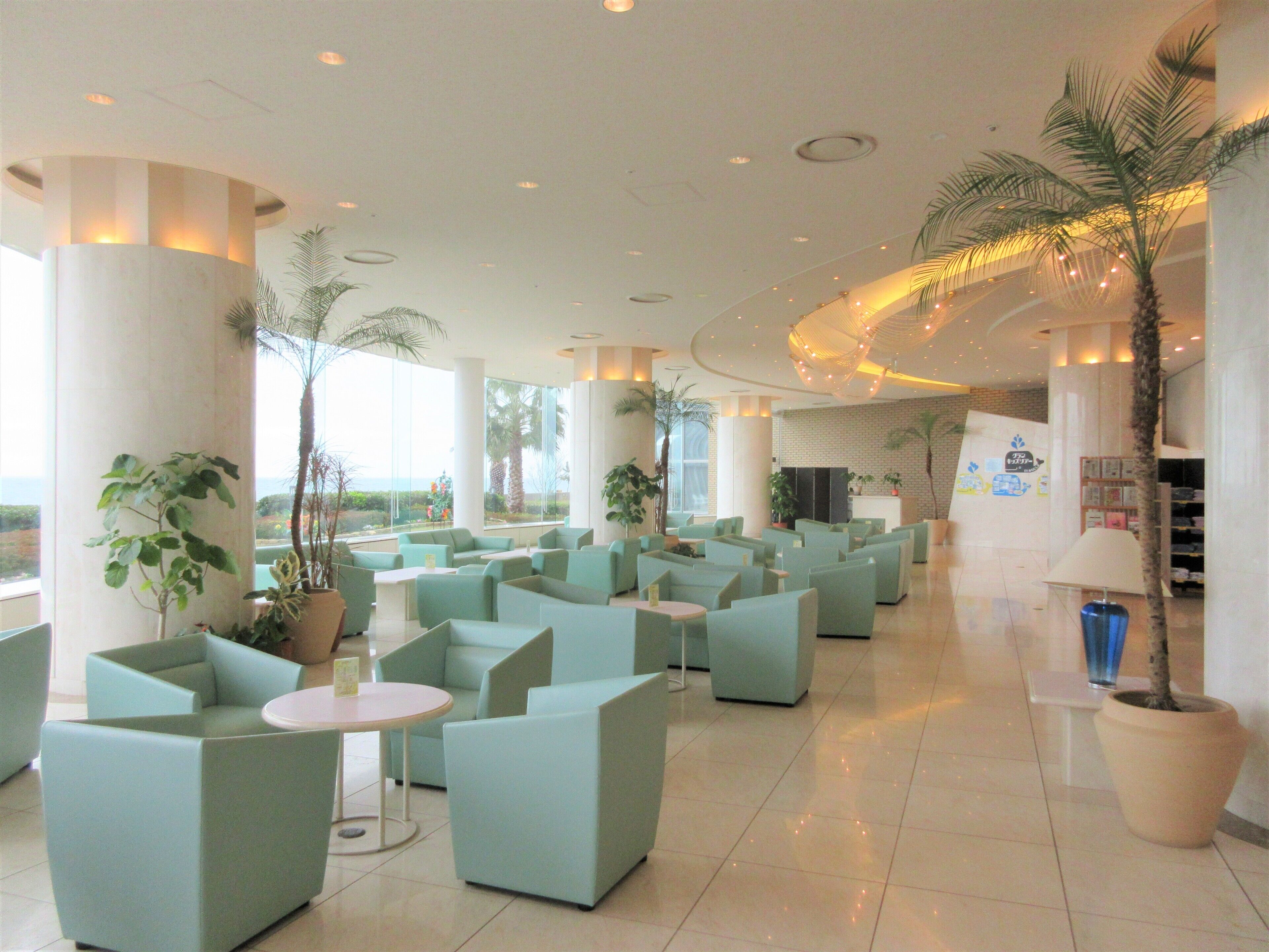 A spacious lobby with multiple seating areas, large windows offering views, and several potted plants.