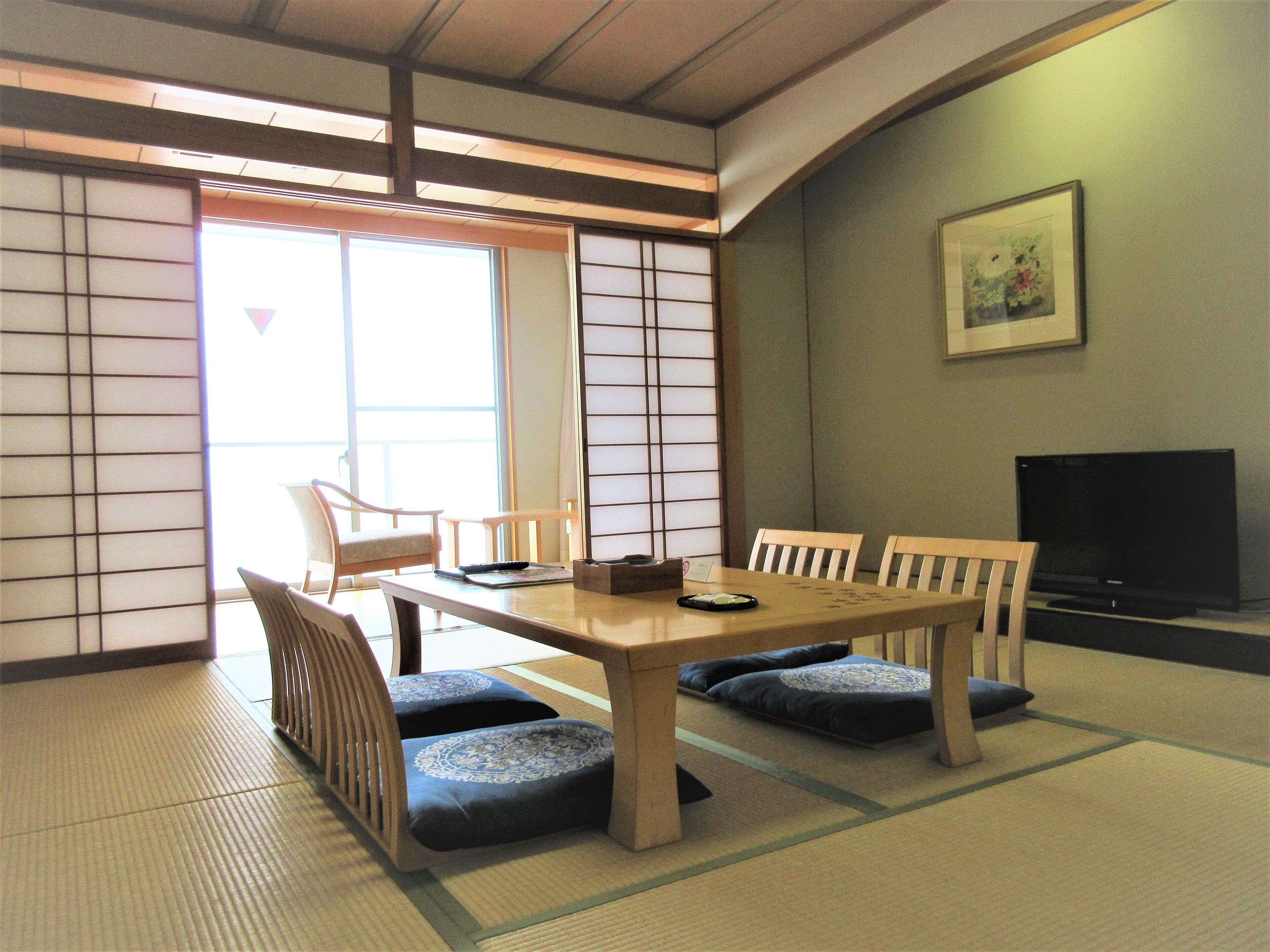 A traditional Japanese-style room with tatami flooring, a low table with cushions, and a television.