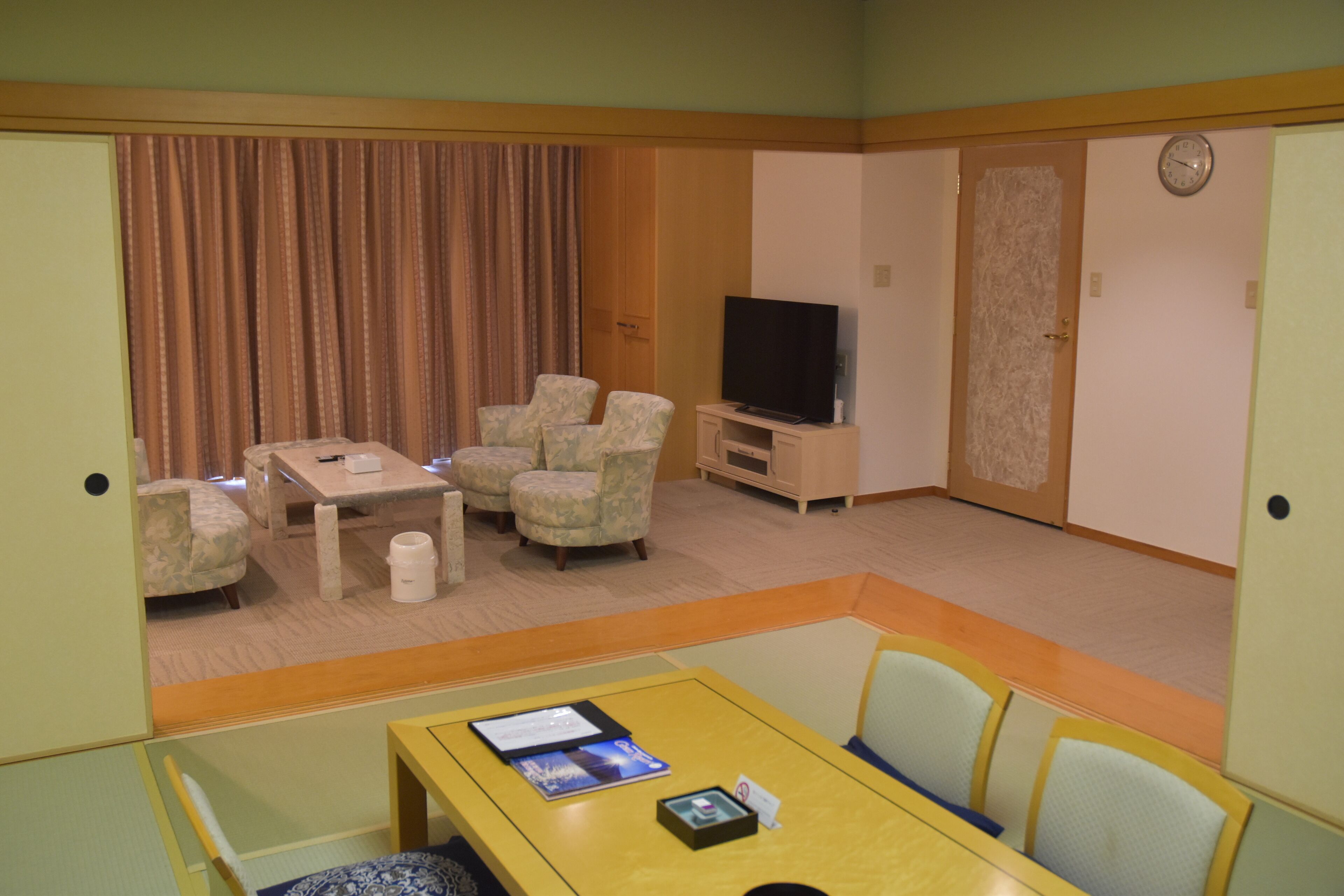 A hotel room with a TV, two armchairs, a small table, and a bed.