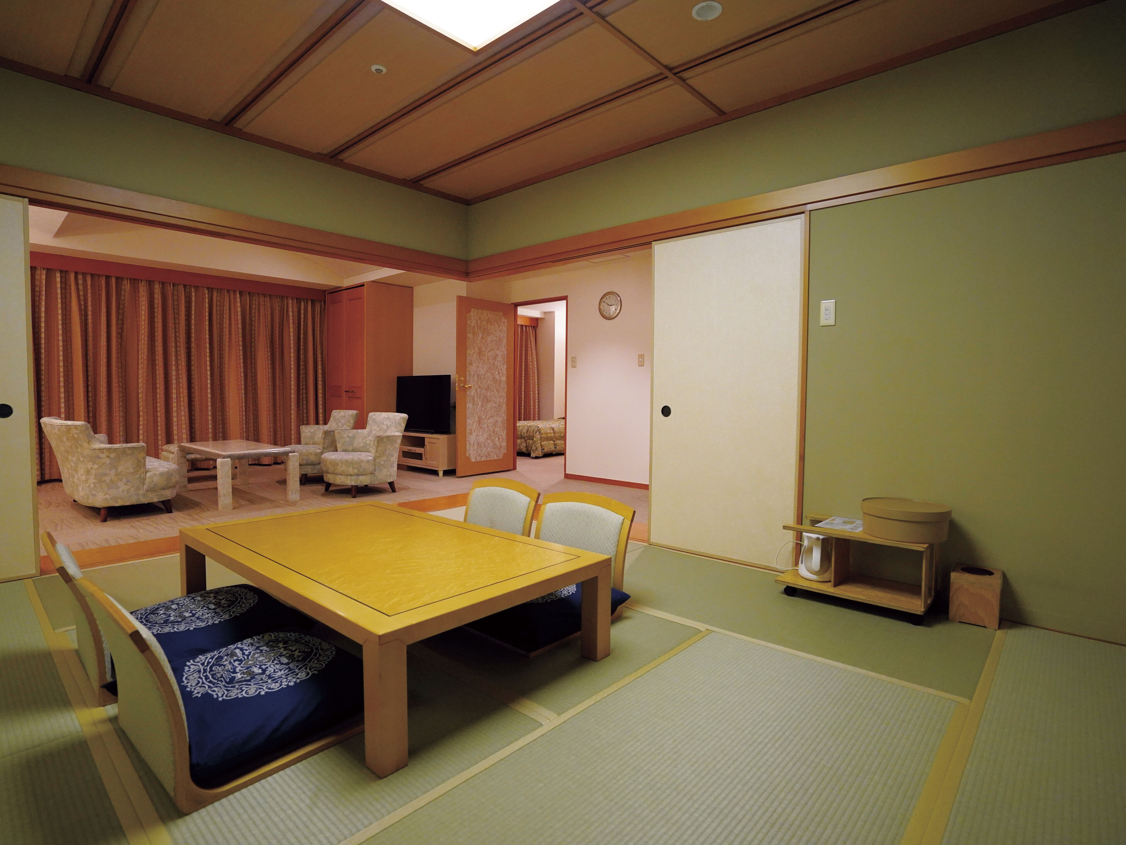 A traditional Japanese-style room with tatami flooring, a low table with cushions, and a television.