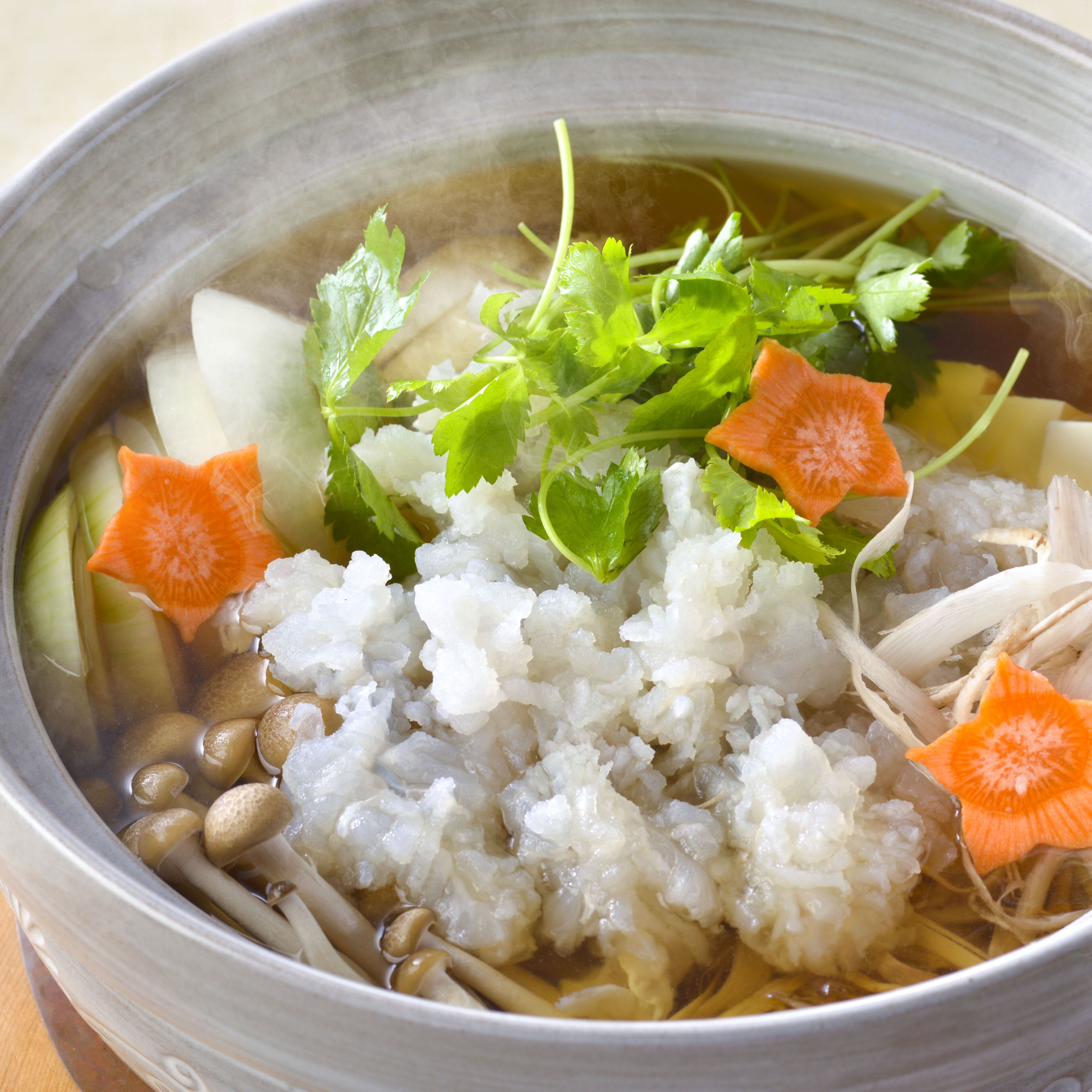 A bowl of clear broth with rice, mushrooms, carrots, and leafy greens.