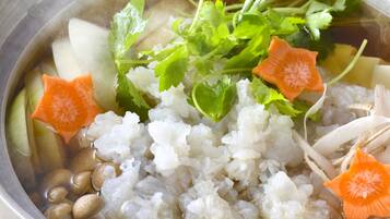 A bowl of clear broth with rice, mushrooms, carrots, and leafy greens.