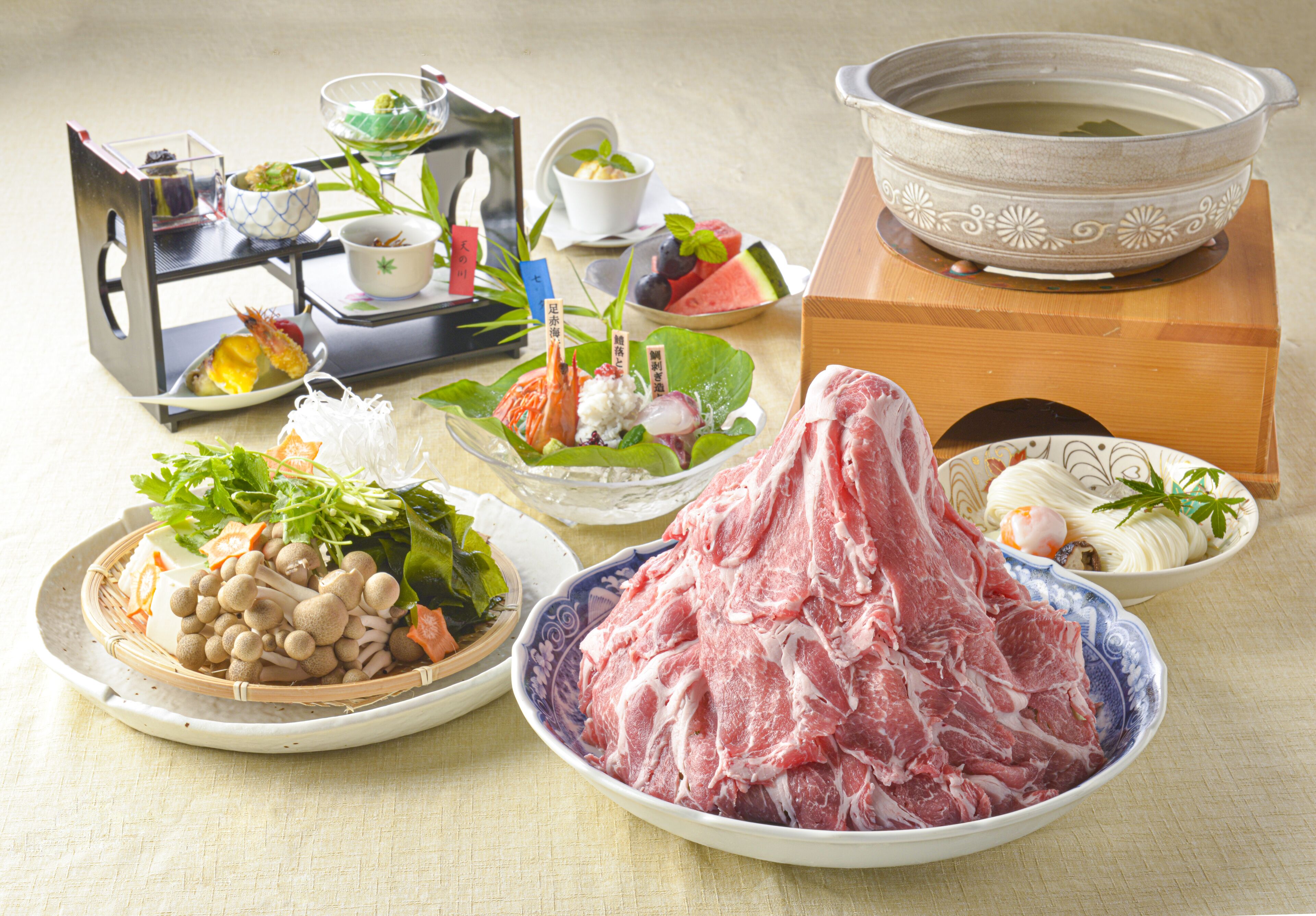 A variety of dishes including raw meat, vegetables, and a bowl of soup, arranged on a table.