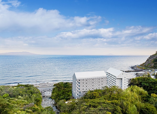 A coastal hotel with a modern design, featuring a prominent white building with a geometric facade, situated on a lush green hillside overlooking the sea.