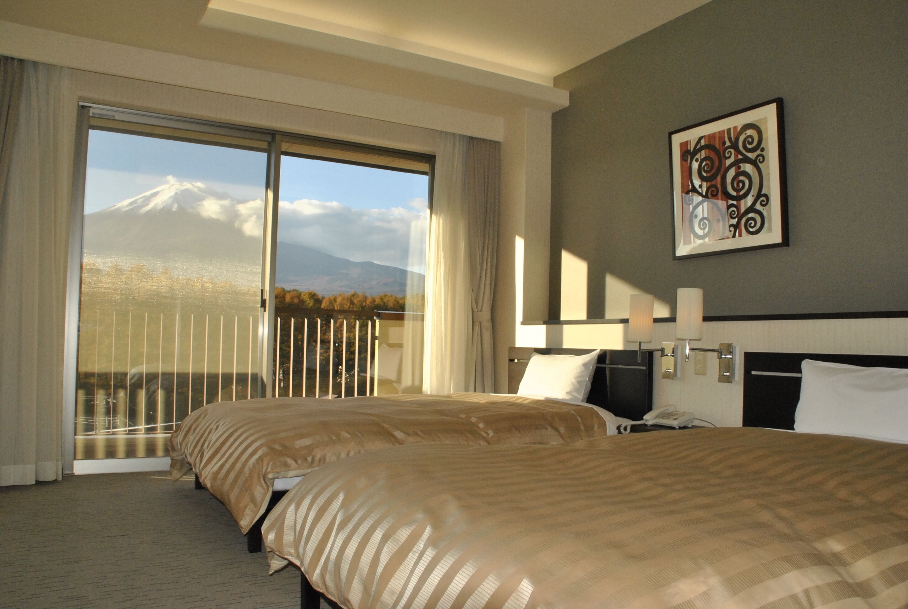 Habitación de hotel con dos camas, un ventanal con vistas a la montaña y un cuadro en la pared.