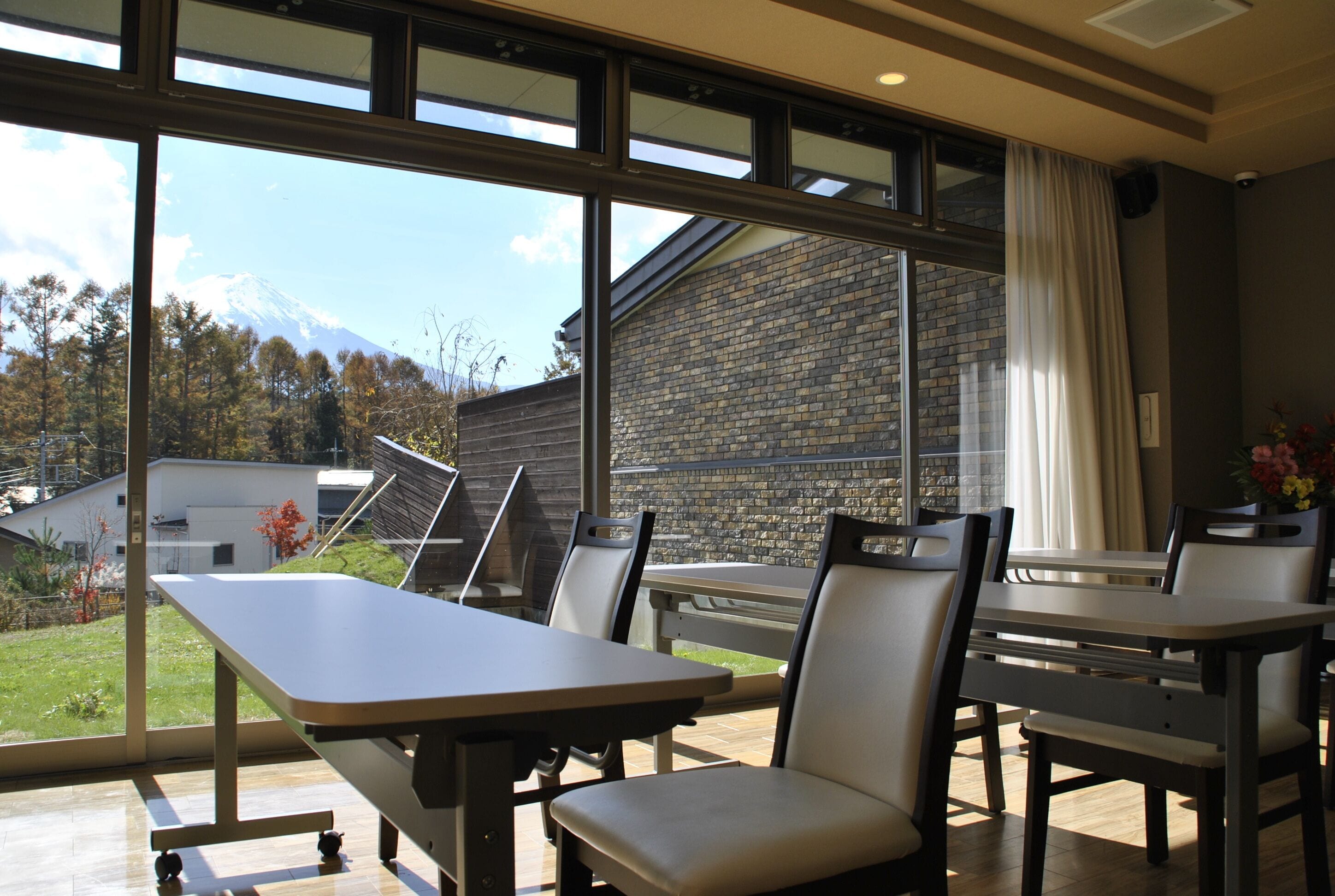 A dining area with a table and chairs, large windows with a view of a mountain and a building, and a brick wall.