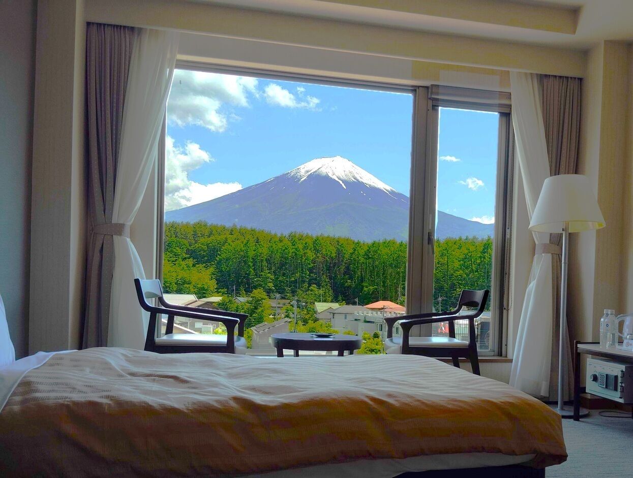 Hotelkamer met een groot bed, twee stoelen, een tafeltje en uitzicht op een berg.