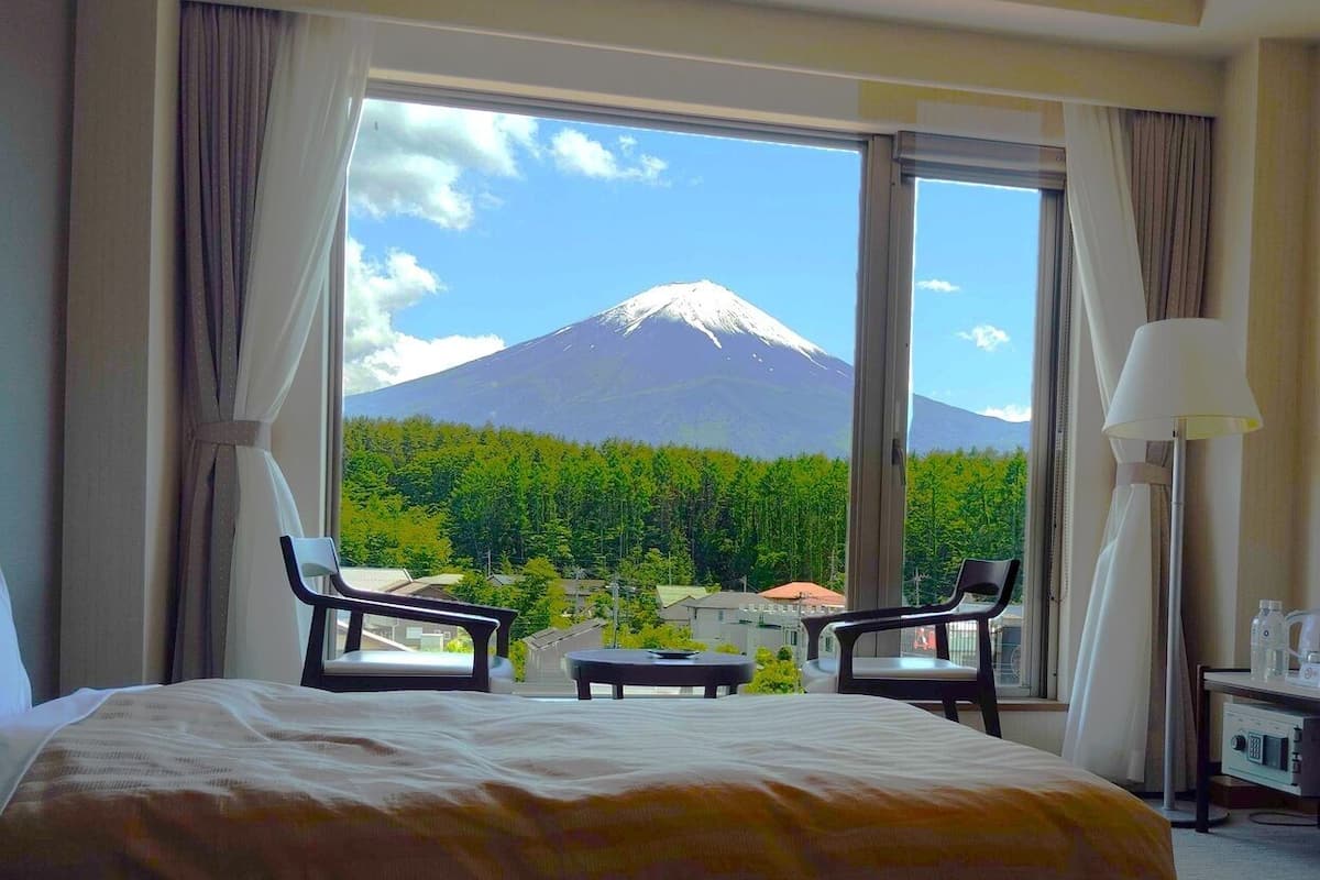 Habitación de hotel con una cama grande, dos sillas, una mesita y vistas a la montaña.