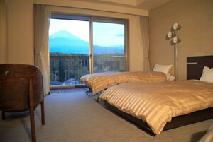 Habitación de hotel con dos camas, una silla y un ventanal con vistas a la montaña.