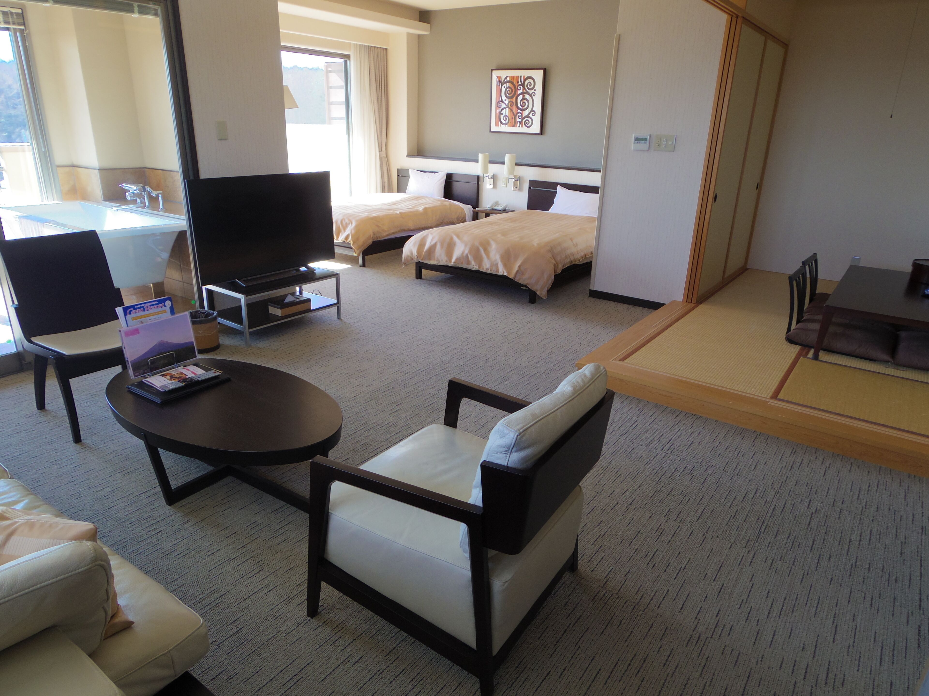 A hotel room with a sofa, a TV, a bed, a dining table, and a tatami mat.
