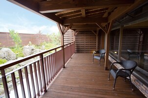 A wooden deck with a railing, two chairs, and a glass enclosure.
