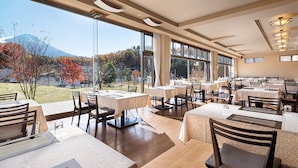 A restaurant with multiple tables and chairs, large windows offering a view of trees and a mountain. - The Gran Resort Princess Fujikawaguchiko (Fujikawaguchiko)