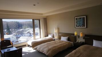 A hotel room with two beds, a chair, a desk, a window with a view of buildings and trees, and a painting on the wall.