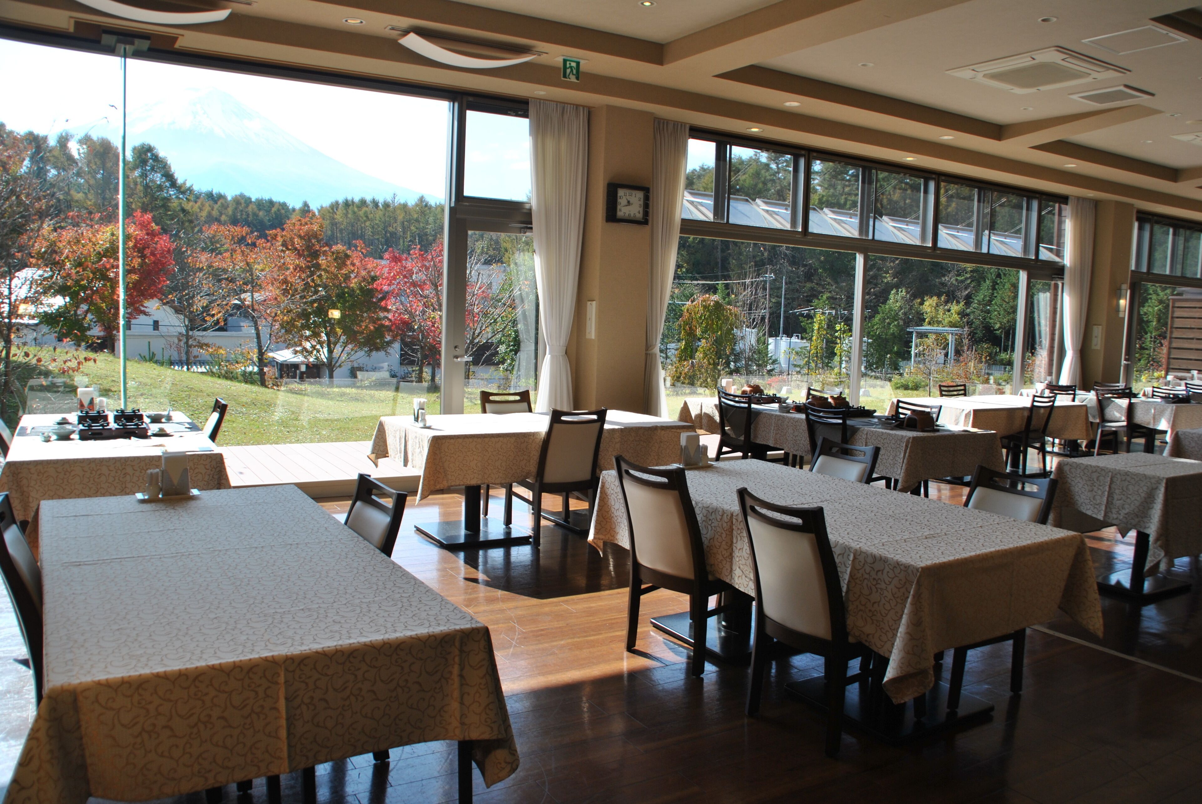A restaurant with multiple tables and chairs, large windows with a view of trees and a mountain.