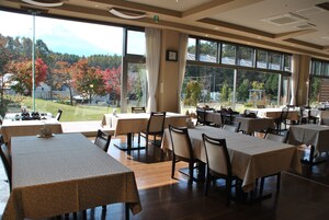 Un restaurante con varias mesas y sillas, amplias ventanas que ofrecen vistas a árboles y una montaña.