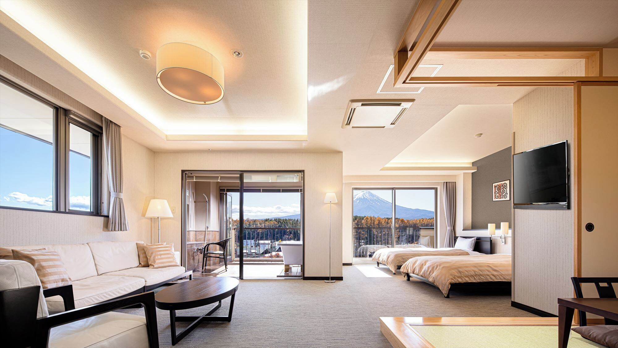Hotelkamer met een bank, salontafel, televisie, bed en balkon met uitzicht op de bergen.