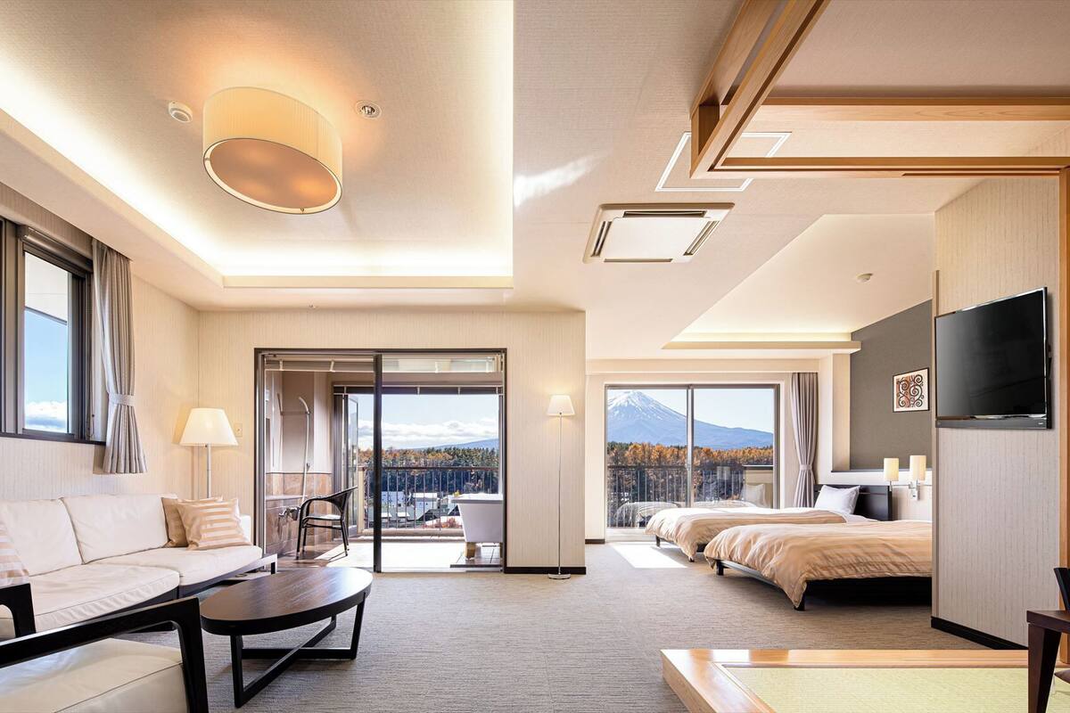 Habitación de hotel con sofá, mesa de centro, televisión, cama y balcón con vistas a la montaña.