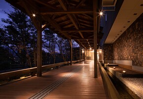 Una terraza de madera con barandillas, un muro de piedra y varios focos.