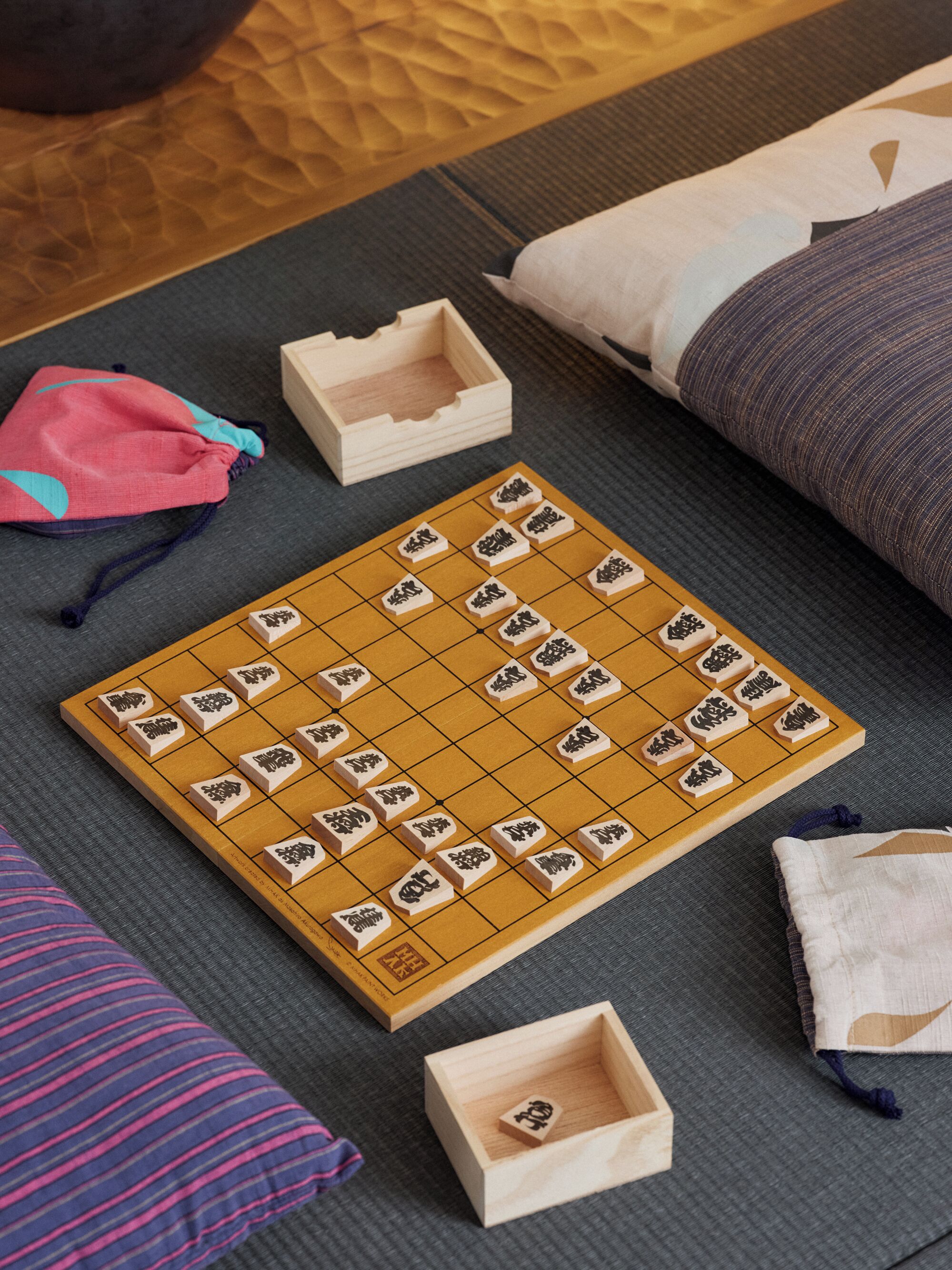 Een Go-bord op een mat met omliggende kussens en een klein houten doosje.