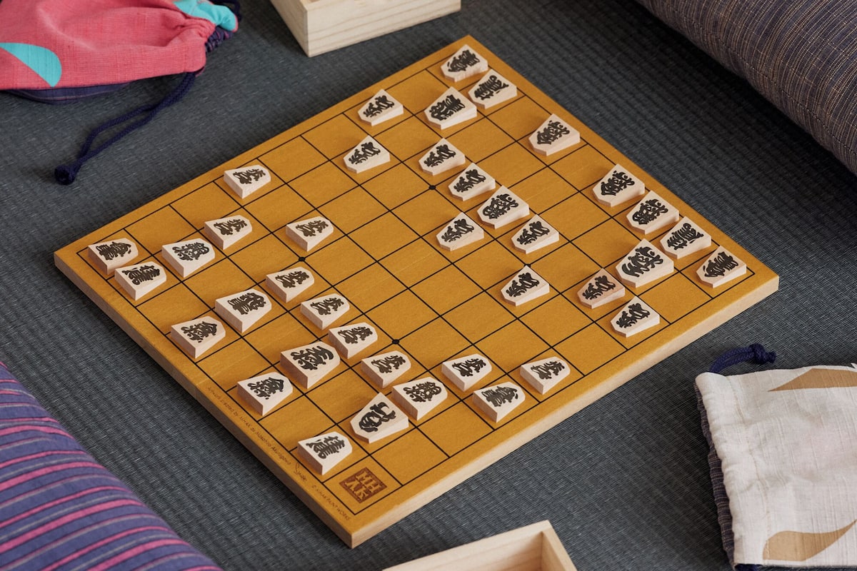 Un tablero de Go sobre un tapete, rodeado de cojines y una pequeña caja de madera.