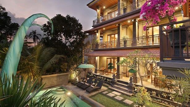 Uma casa de dois andares com varanda, piscina e um jardim com plantas tropicais.