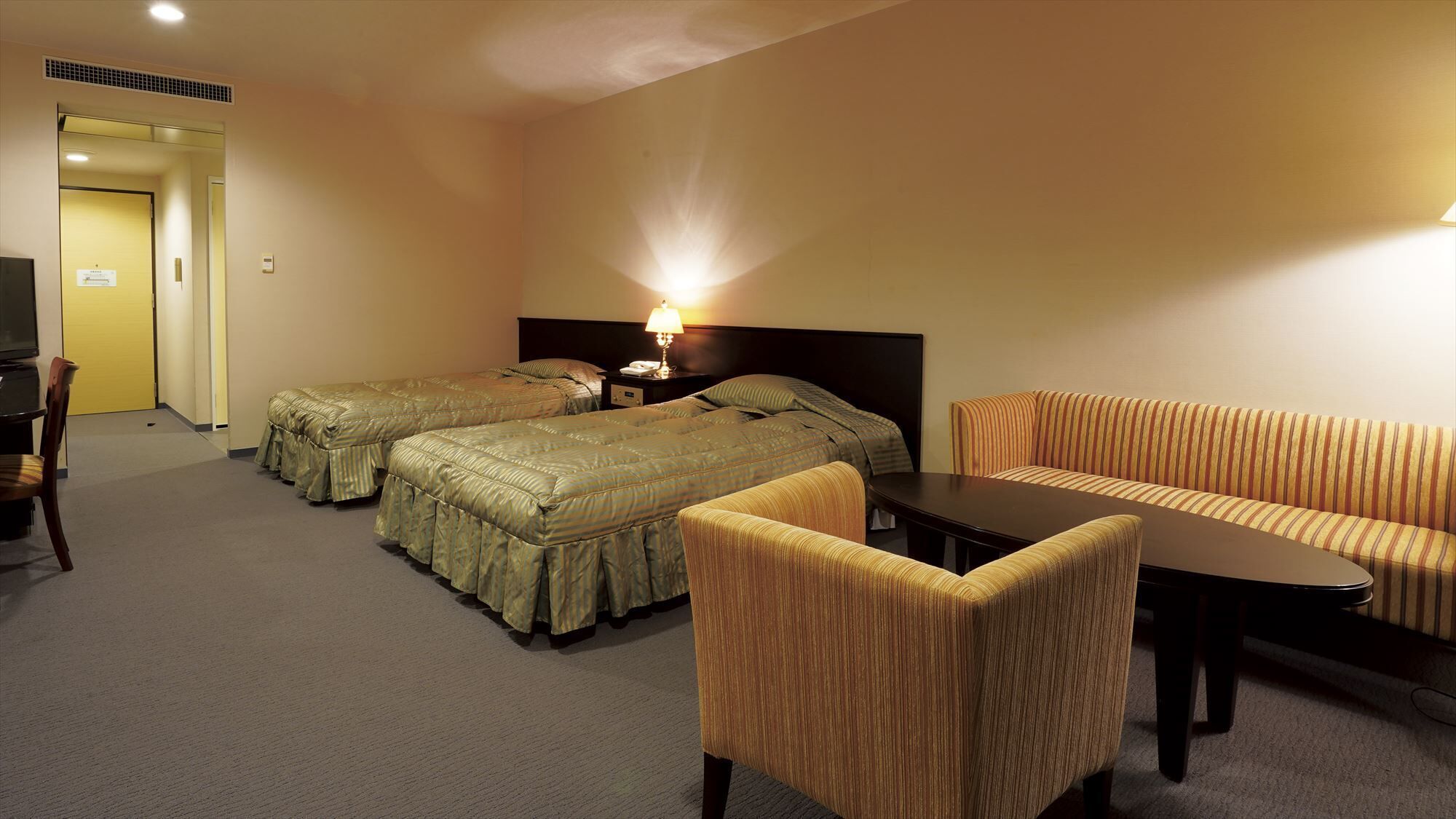 A hotel room with two beds, a sofa, a table, and a chair.