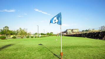 Camp de golf amb una bandera blava marcada amb una ‘A’ blanca en un penya-segat, envoltat d'un tapet verd ben cuidat i parets de pedra.
