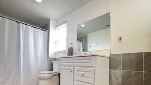 A bathroom with a toilet, a white vanity with a mirror, a shower curtain, and a patterned rug. - Spring Lake Manor - Rutgers | NYC | Middlesex County New Jersey - EXTENDED STAY (South Plainfield)