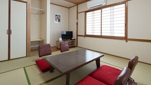 A traditional Japanese room with tatami flooring, a low wooden table, red cushions, a television, and a sliding door. - Tabist Beppu kitahama no yado ao (Beppu)